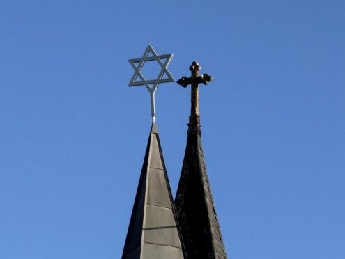 Två kyrktorn med Davidsstjärnan på det ena och ett kors på det andra.